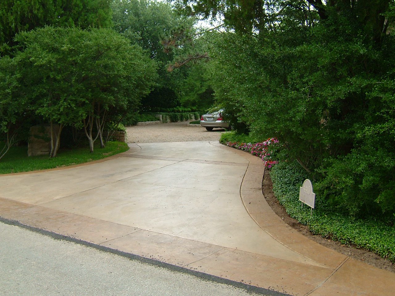 Curved concrete driveway with parked car among trees